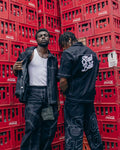 Two men standing on a wooden pallet among stacked red crates.