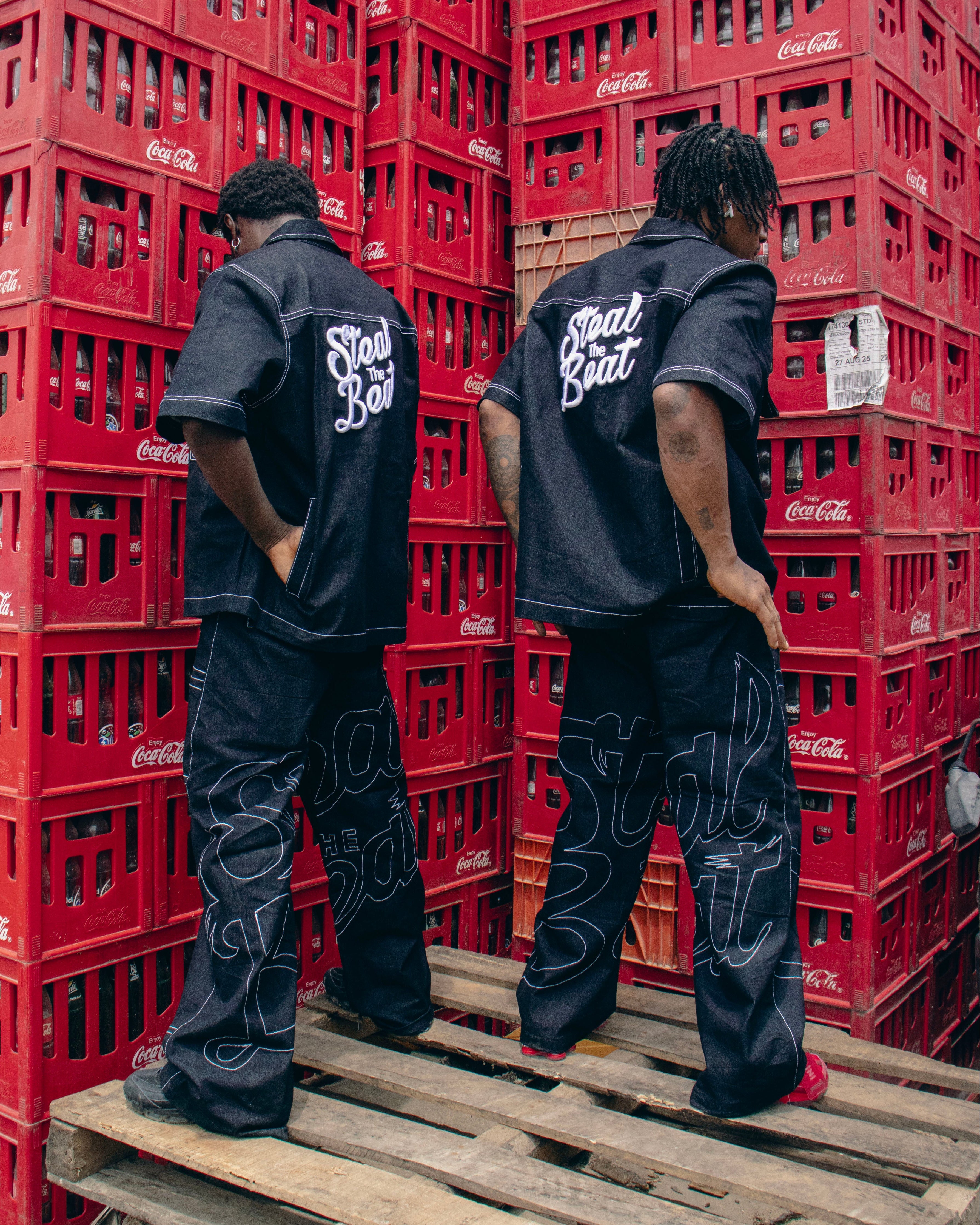 Two people wearing black outfits with 'Red Bull' branding standing between red crates.